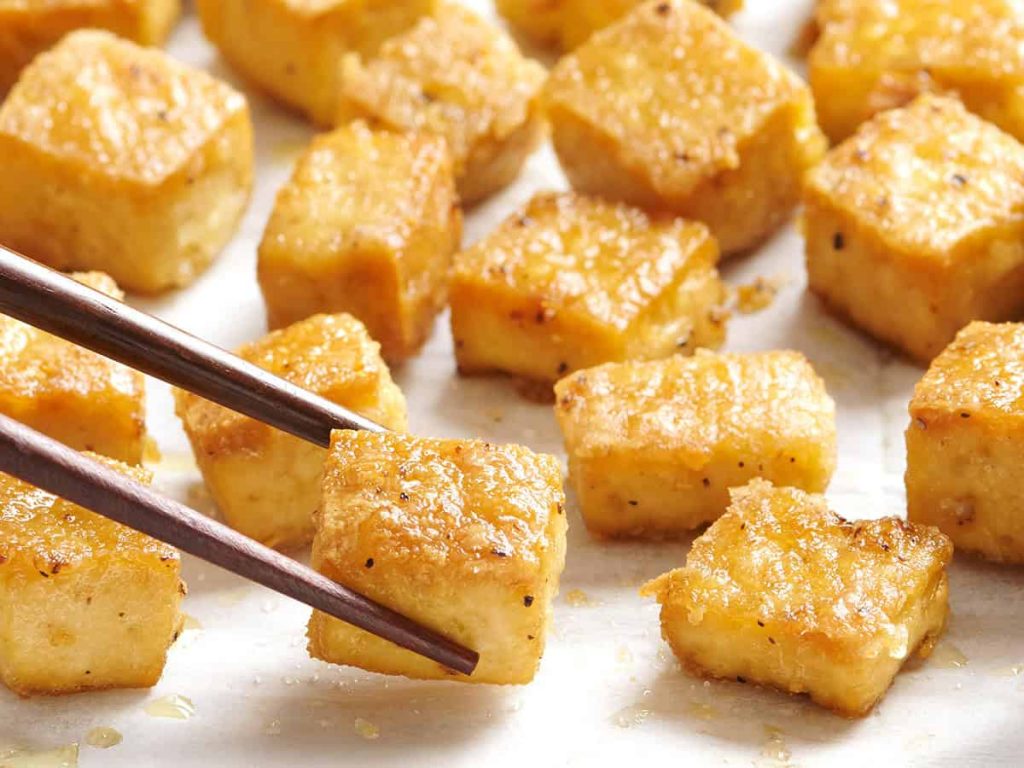Overed view of baked tofu being picked up with chopsticks.