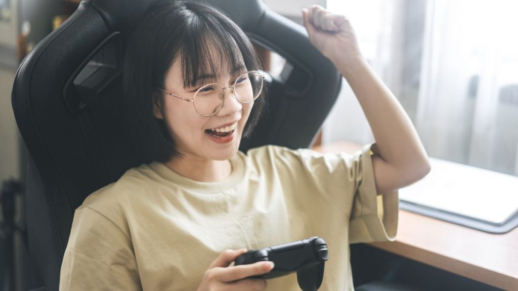 Young Adult With Glasses Sitting On A Gaming Chair Holding A Game Controller
