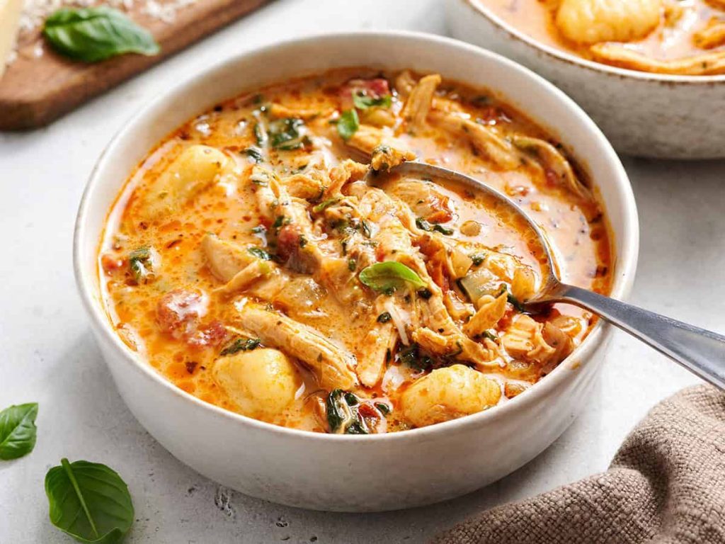 Marry me chicken soup in a white bowl with a spoon, garnished with fresh basil.