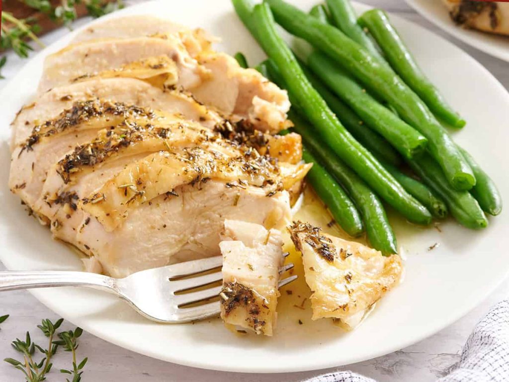 A herb roasted chicken breast with green beans on a plate with a fork.