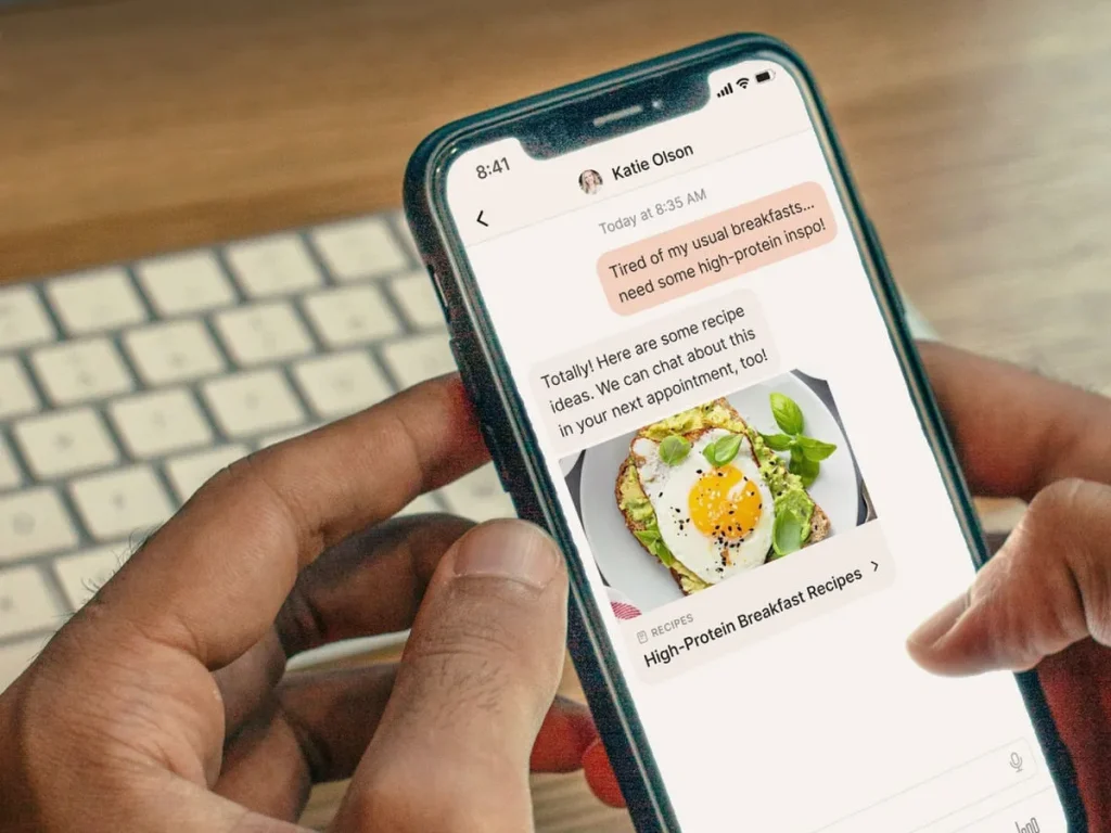 A $0 Online Dietitian to Support Weight Loss, Hormone Changes & More?! Yes, Really! holding a phone showing a nutrition app in front of a keyboard