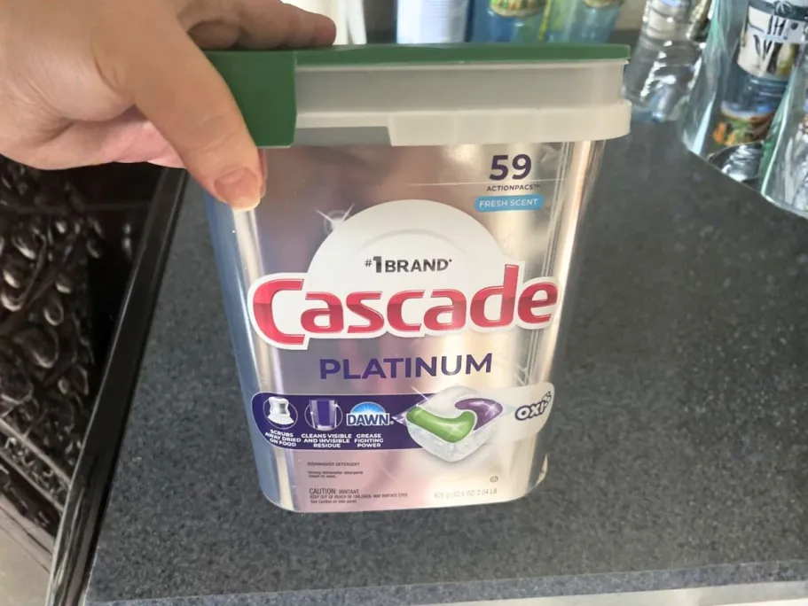 THREE Cascade Platinum Dishwasher Pod 59-Packs Only $37.47 Shipped After Rebate (Reg. $60) hand holding Cascade Platinum + Oxi Dishwasher Pods 59-Count package in kitchen