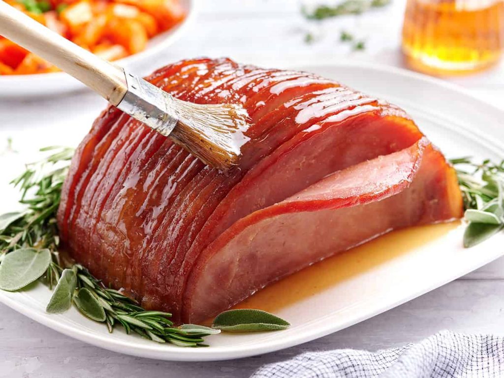Honey Glazed Ham – Budget Bytes Honey glazed ham on a plate with herbs, being brushed with glaze.