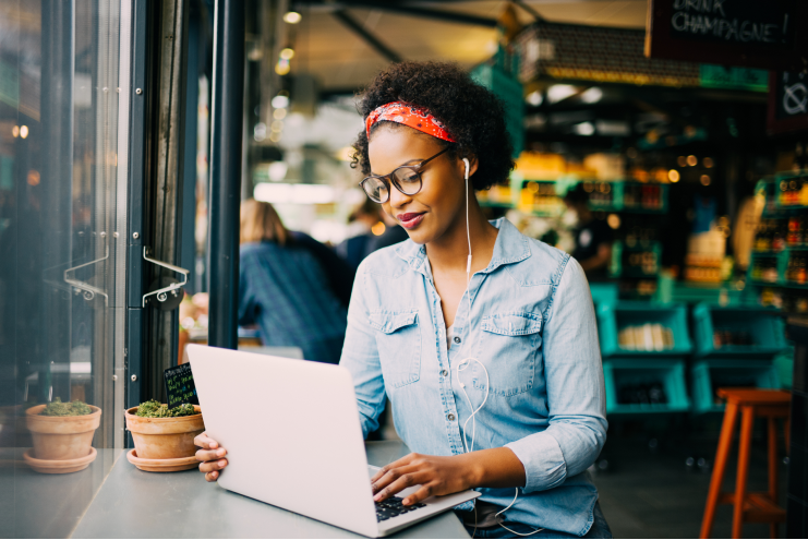 Why Are Small Business Owners Choosing Quicken Business & Personal? Focused young woman sitting alone at a counter in a cafe working on a laptop and listening to music on earphones